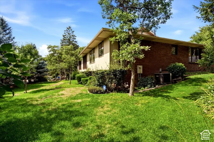 Expansive grassy yard with mature trees, brick and siding exterior, and well-maintained shrubbery