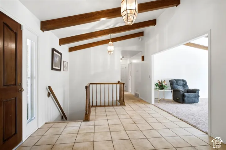 Vaulted ceiling with exposed wood beams, tile flooring, wood-paneled entry door, sidelight window, and a wood banister