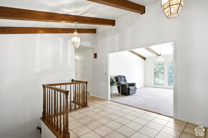 Vaulted ceiling with exposed wood beams, tiled flooring, wooden staircase railing, and recessed lighting