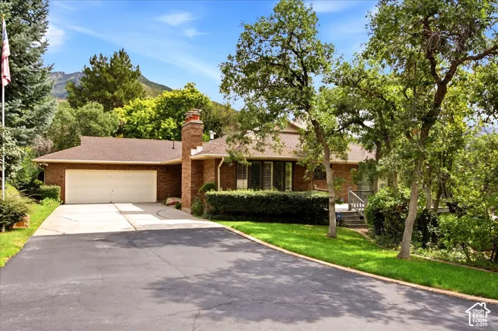 Brick exterior residence featuring a two-car garage, asphalt driveway, concrete entry path, and mature landscaping