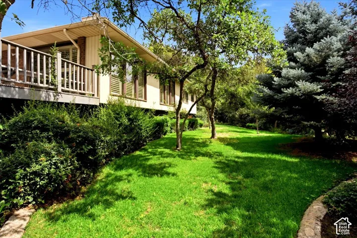Exterior featuring a balcony with wood railing, large windows with shutters, and mature landscaping