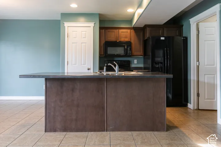 Kitchen island with a built-in sink, wood-finish cabinetry, black appliances, and recessed lighting
