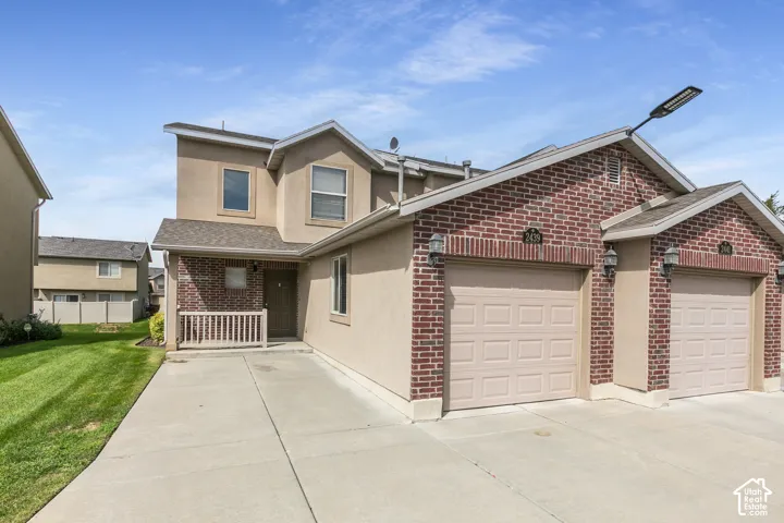 Two-story exterior featuring brick and stucco finishes, attached garages, a covered front entry, and a concrete driveway