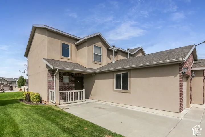 Multi-story property featuring a stucco and brick exterior, a covered front porch with white railings, a paved driveway, and an attached garage with a brick-framed entrance