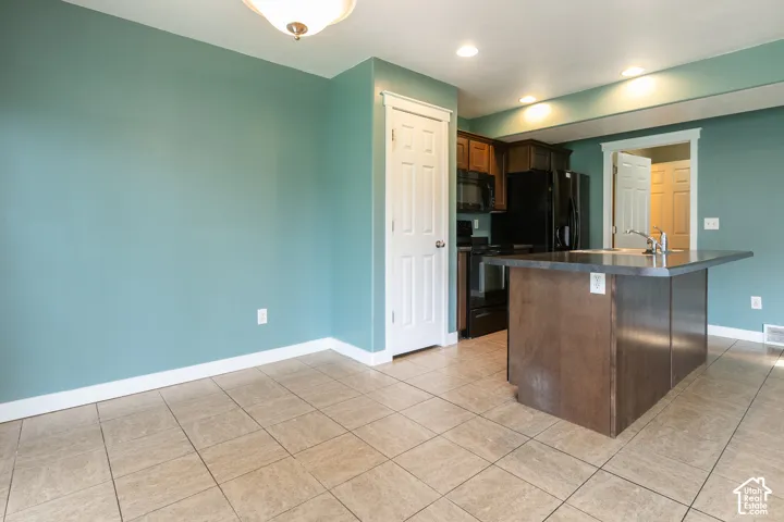 Tiled flooring, central island with integrated sink, dark wood-finish cabinetry, recessed ceiling lighting, and black appliances