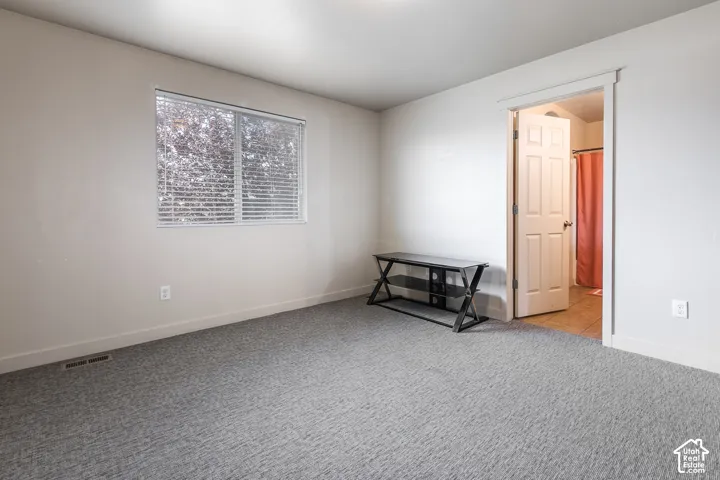 Light-toned walls, gray patterned carpeting, and a window with horizontal blinds