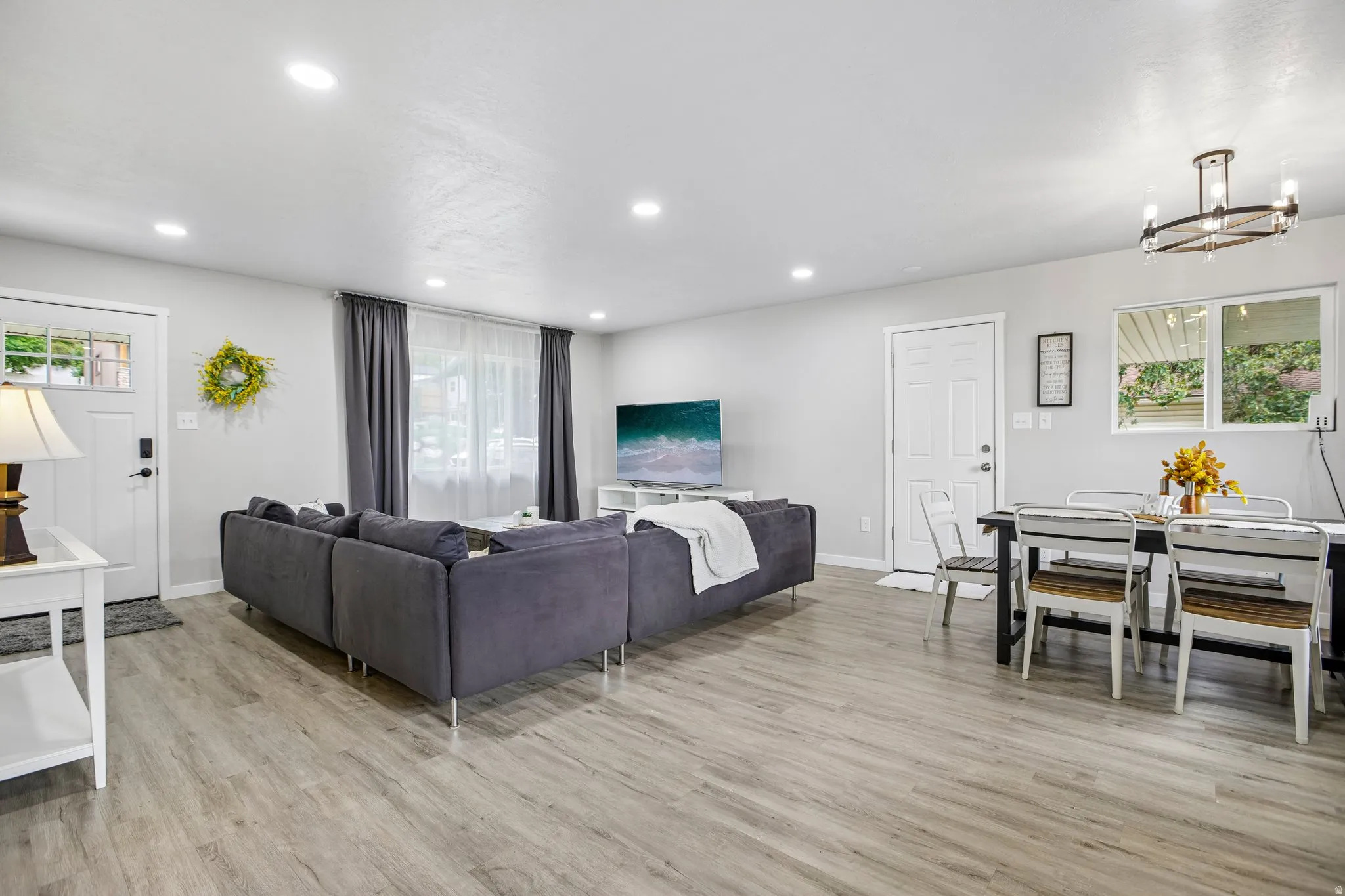 Open-concept living area featuring wood-finish flooring, recessed lighting, and a white paneled entry door