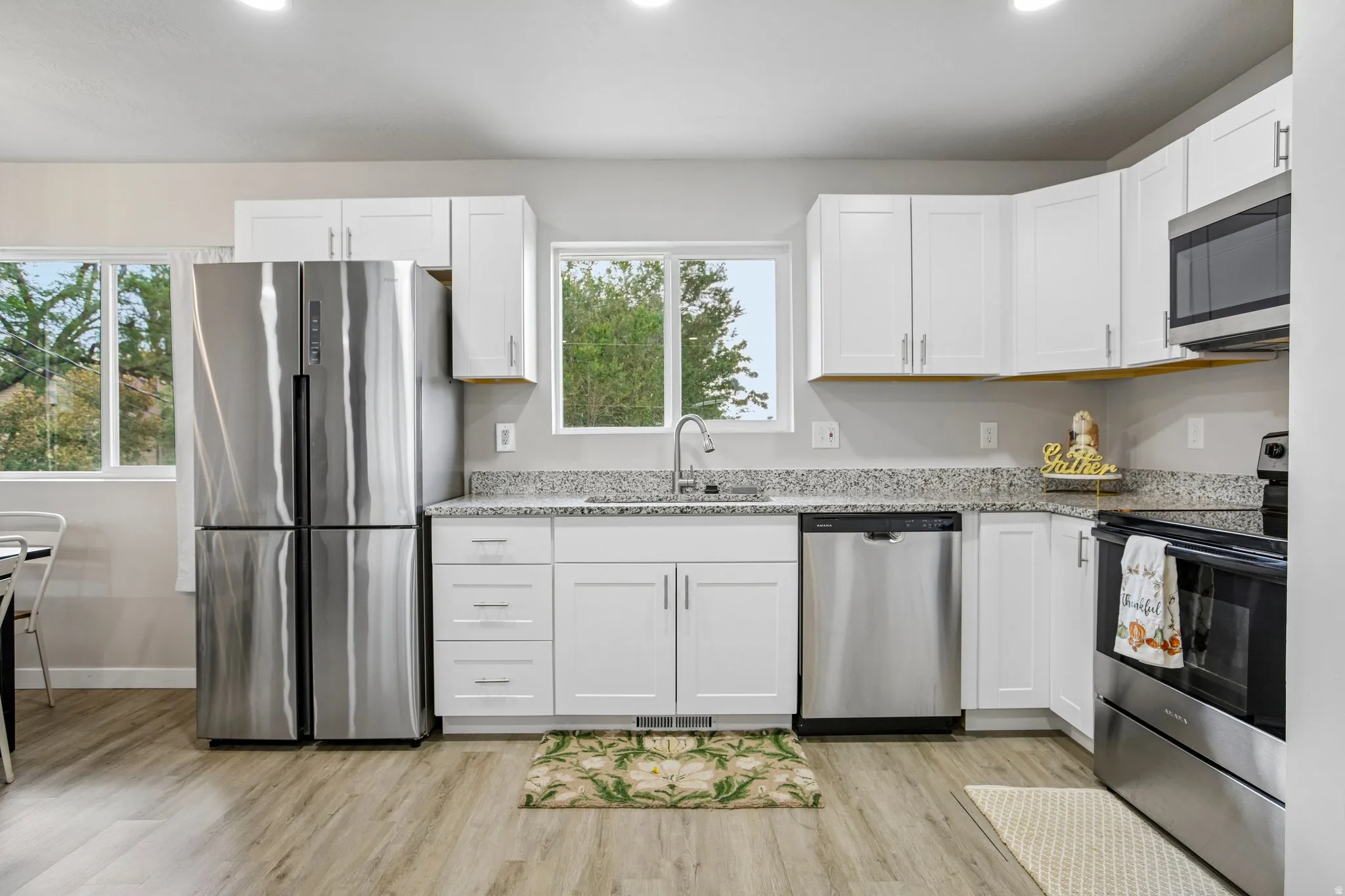 Modern kitchen featuring white cabinetry, stainless steel appliances, speckled countertops, and wood-finish flooring
