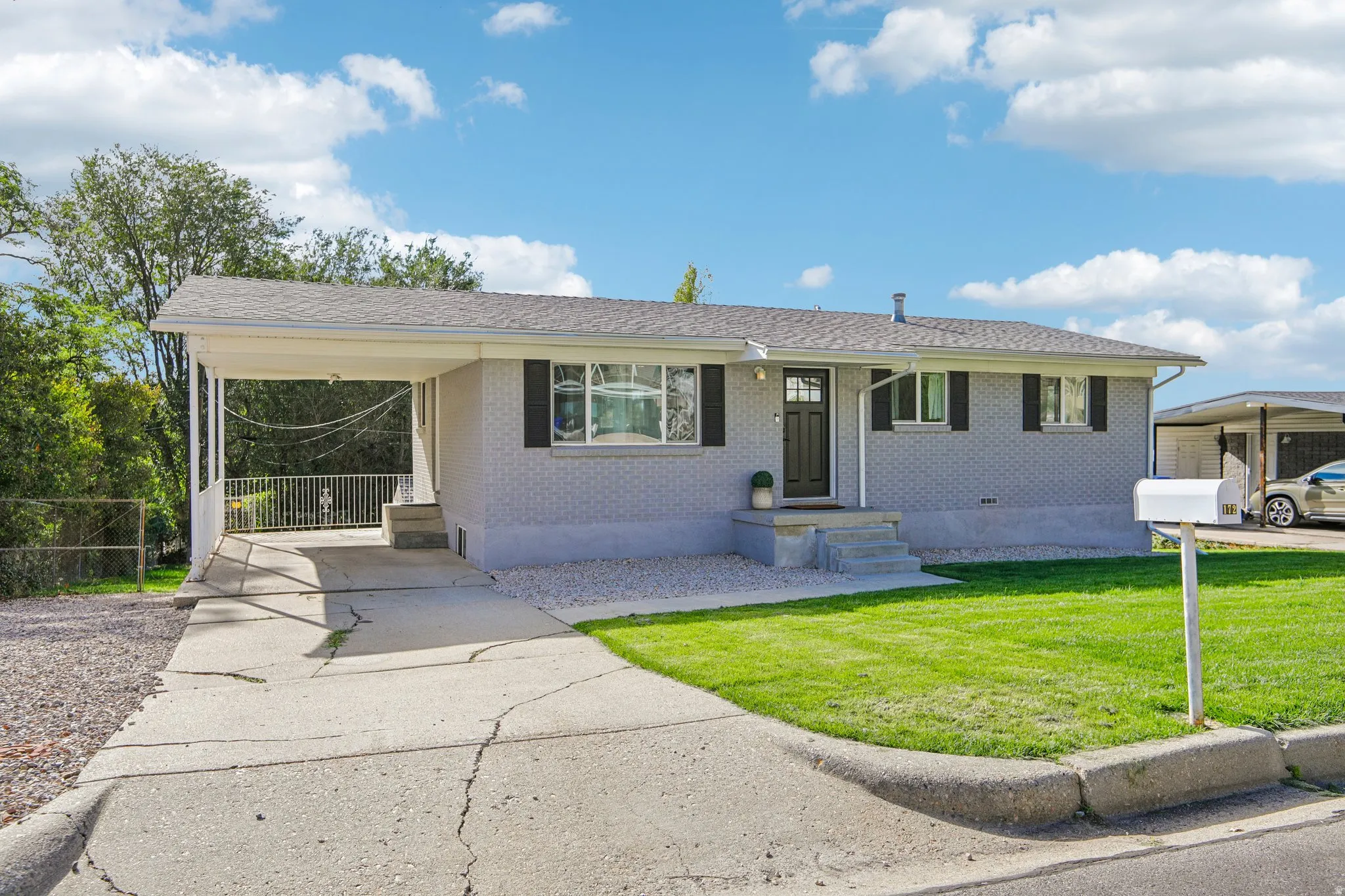 Light gray brick exterior with a front entry porch, black front door, and a covered carport