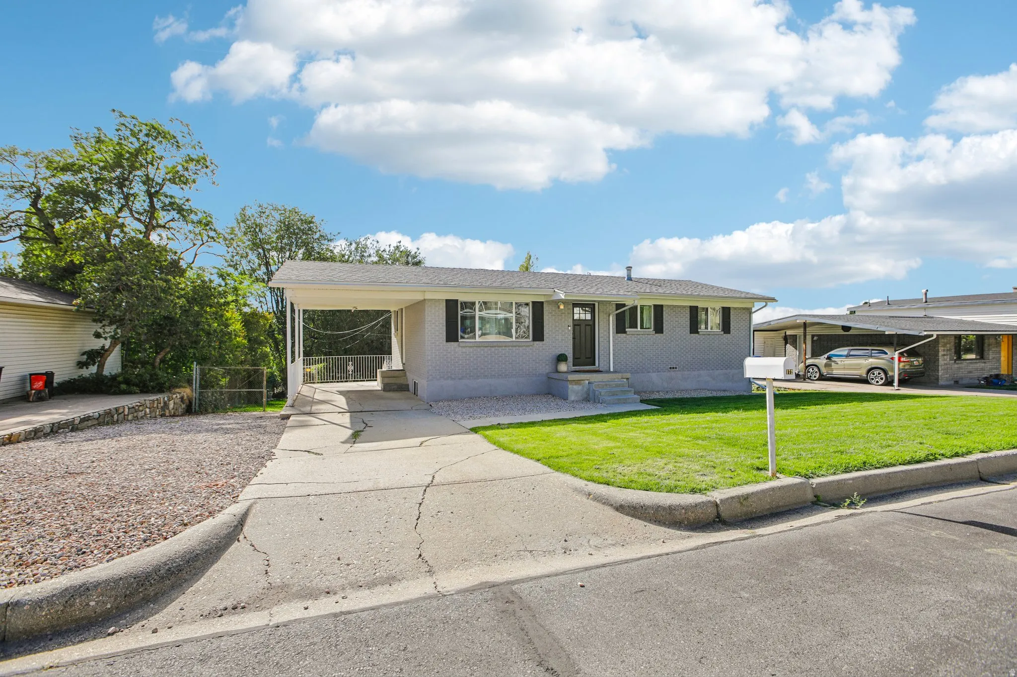 Single-story exterior with light gray brick, black window shutters, and a carport