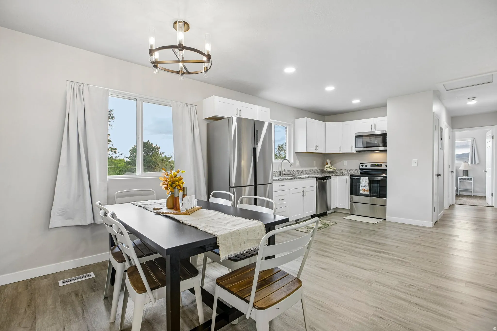 Open concept layout with wood-finish flooring, white cabinetry, stainless steel appliances, and recessed lighting