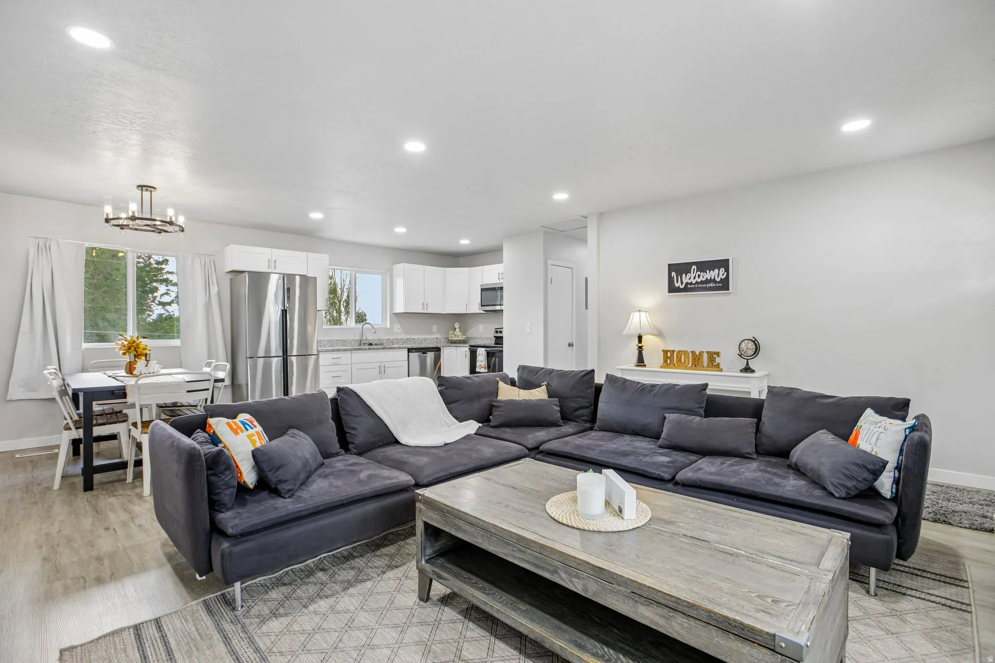 Open-concept living area featuring wood-finish flooring, recessed lighting, and a modern kitchen with stainless steel appliances and white cabinetry