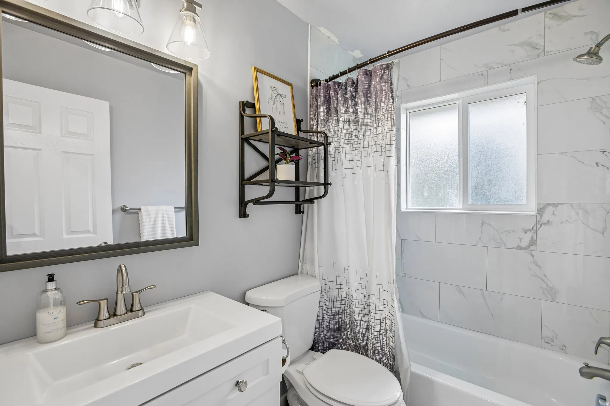 Bathroom featuring a single vanity, framed mirror, light gray wall paint, and white subway tile bath surround