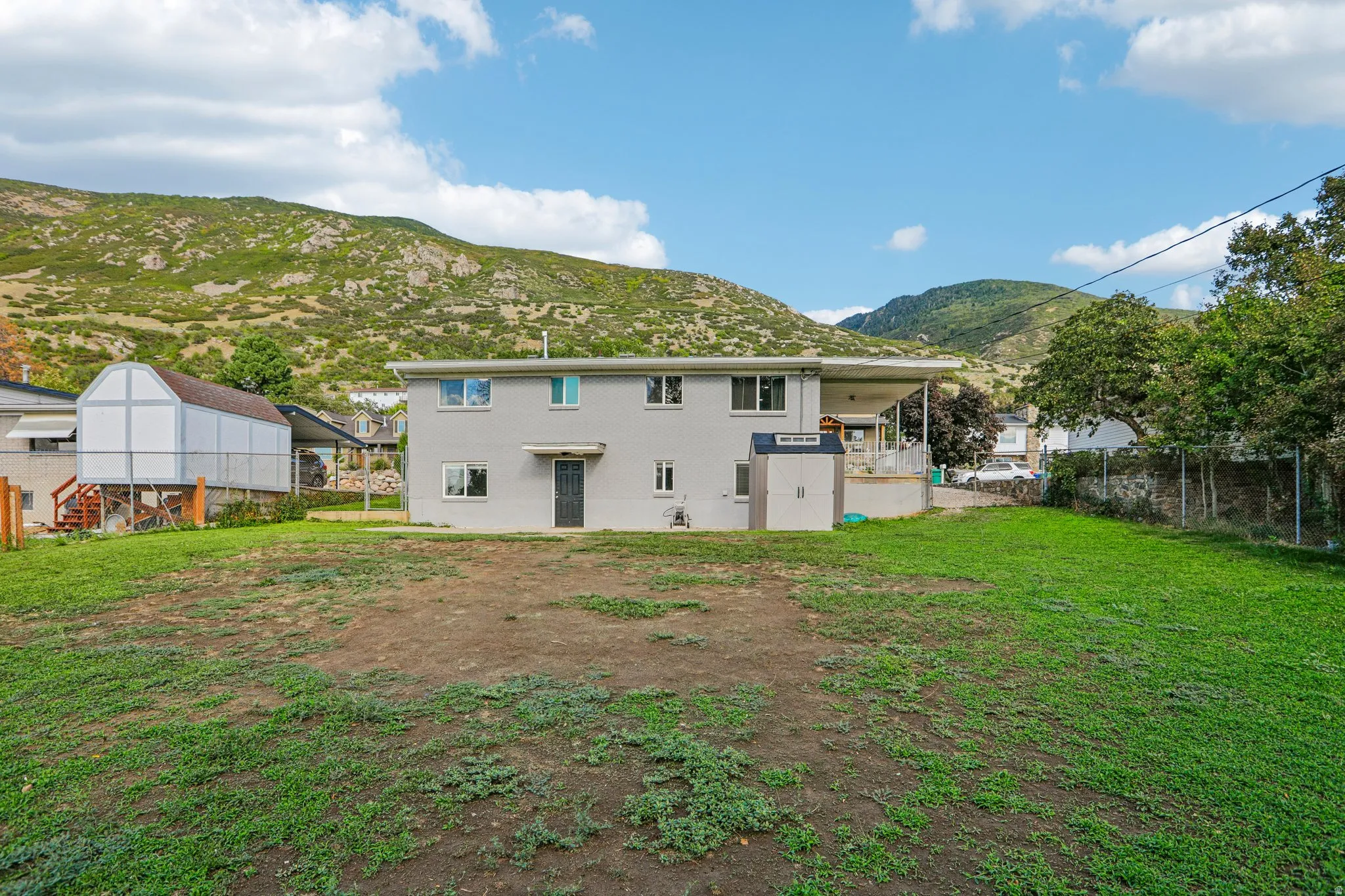 Expansive backyard with a two-story residence featuring a covered patio, exterior storage shed, and a detached outbuilding
