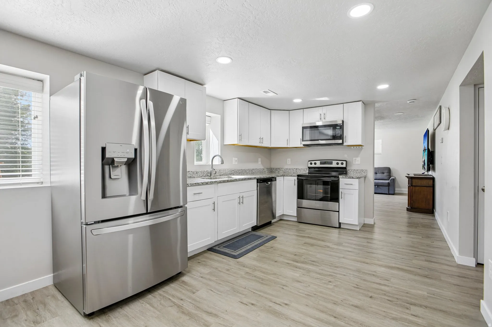 Kitchen featuring white cabinetry, light-toned countertops, stainless steel appliances, and wood-finish flooring