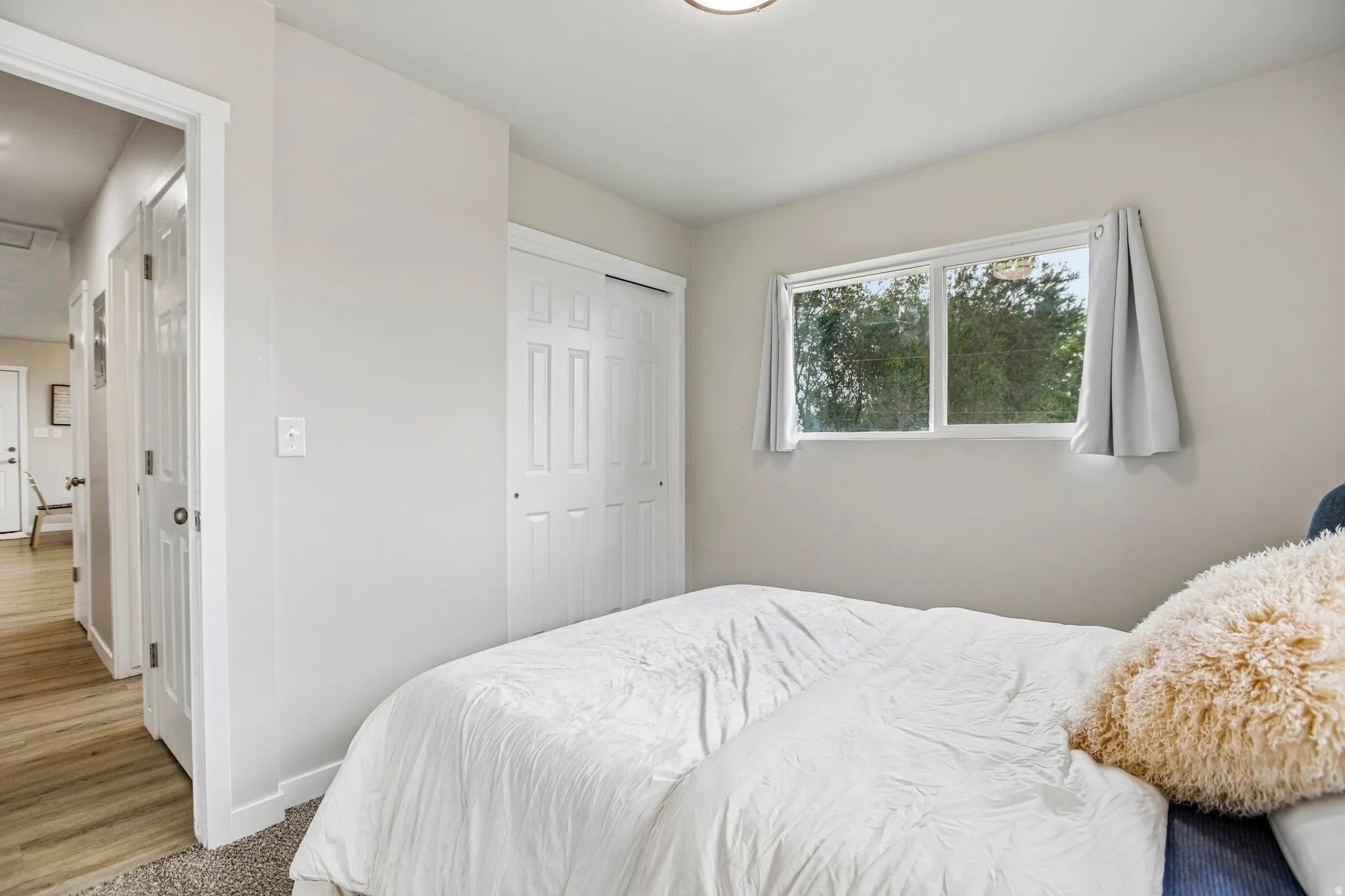 Window with exterior foliage, white bi-fold closet doors, neutral wall paint, and carpet flooring