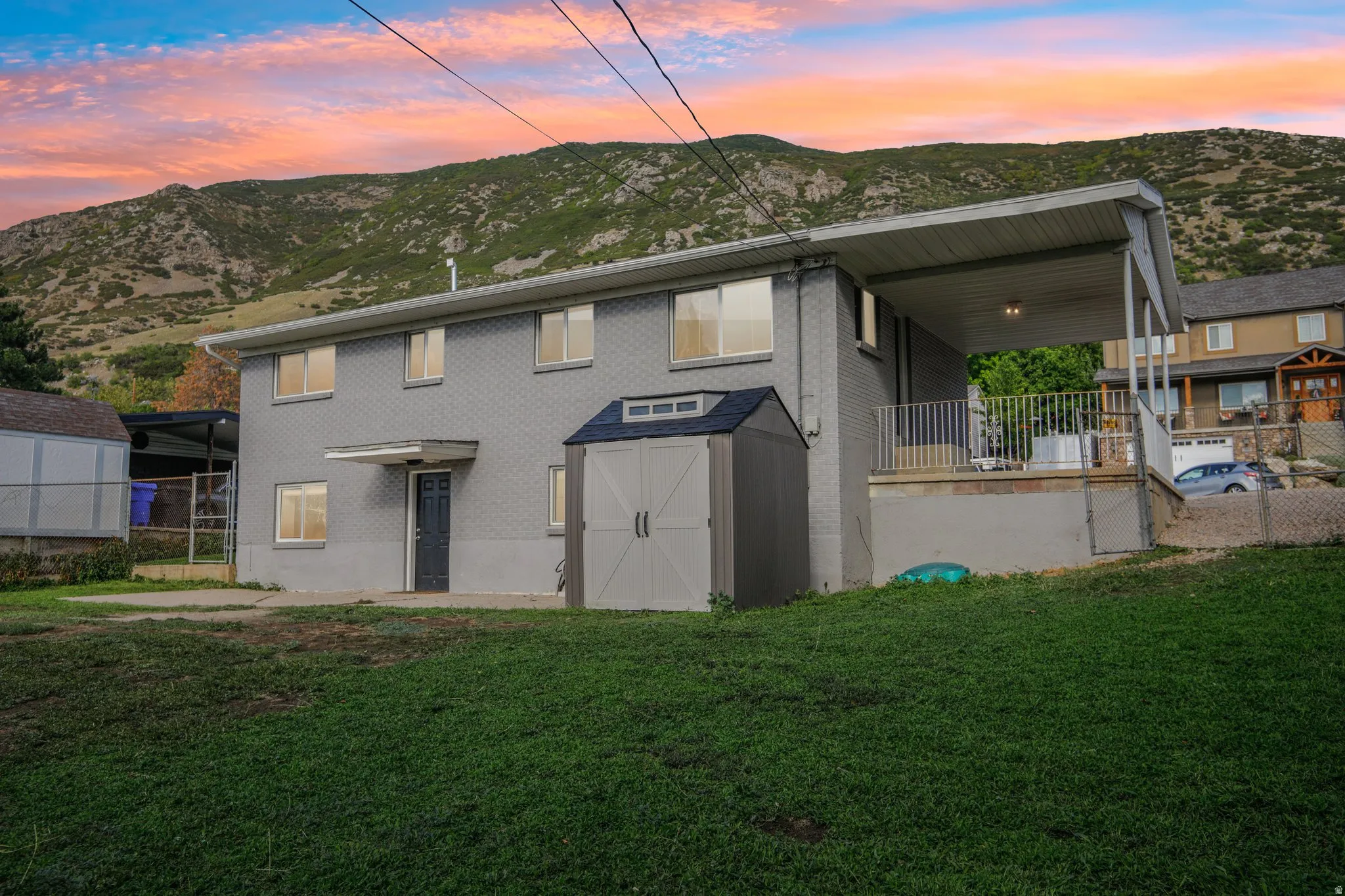 Two-story exterior with a covered carport, elevated patio with metal railings, and a storage shed