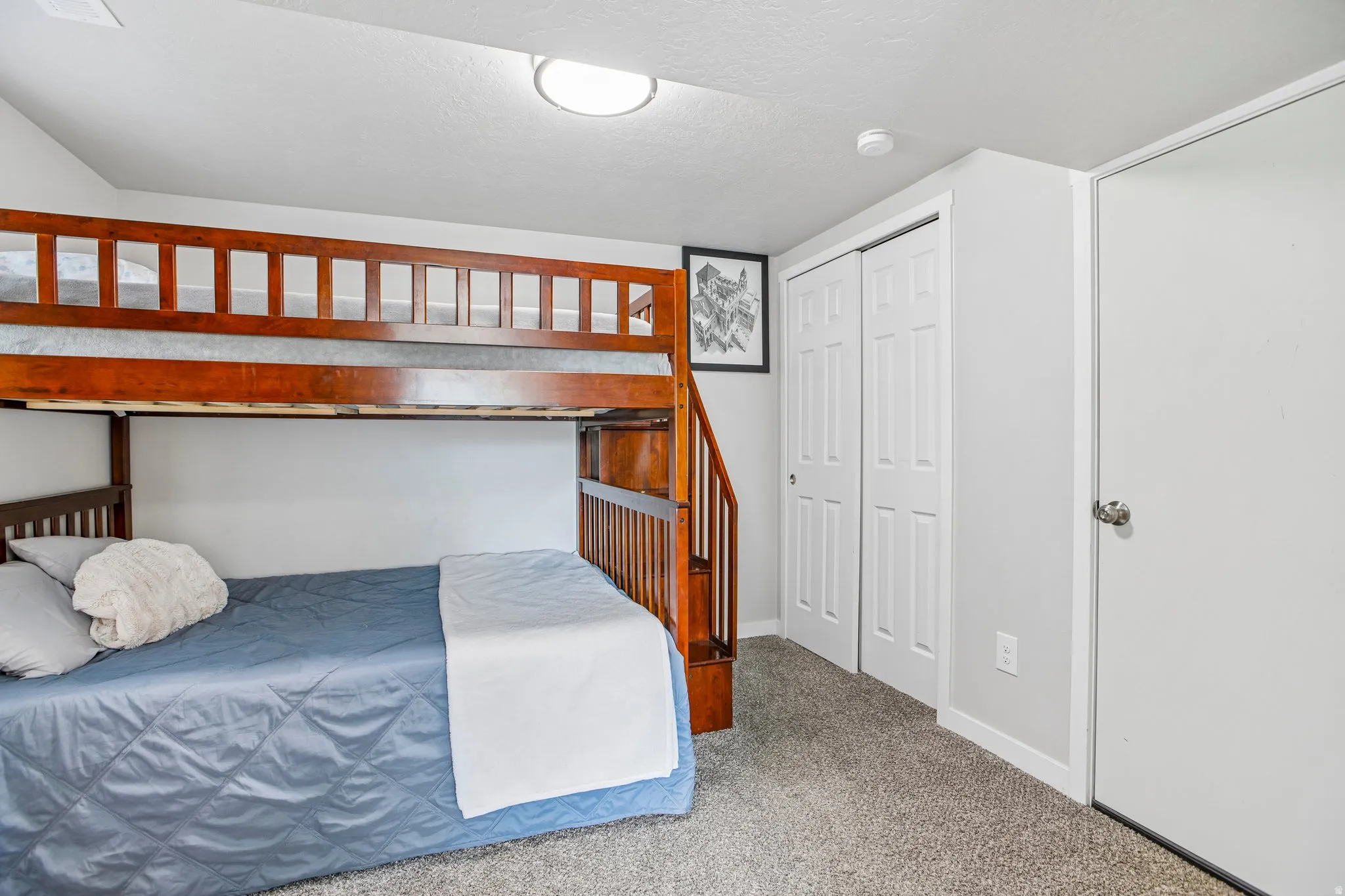 Carpeted room featuring a built-in wooden bunk bed structure with an integrated staircase, white bi-fold closet doors, a white solid door, and a flush-mount ceiling light fixture