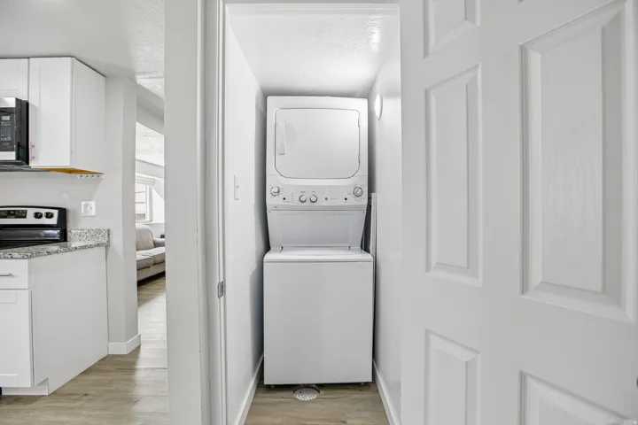 Stacked washer and dryer unit, wood-finish flooring, white paneled door, recessed lighting, and a floor drain