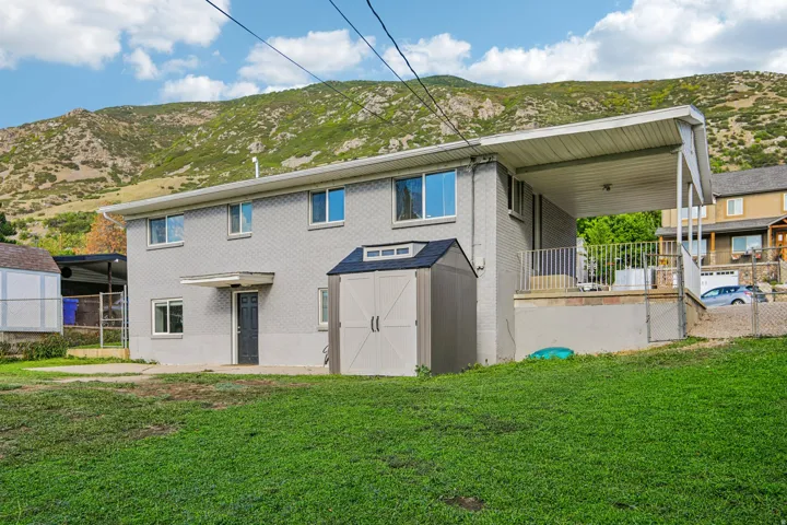 Two-story exterior with a covered porch, an additional storage shed, and a mountain backdrop