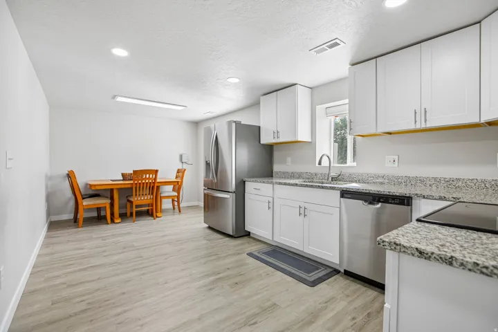Kitchen featuring white cabinetry, light-toned wood-finish flooring, stainless steel appliances, and stone countertops