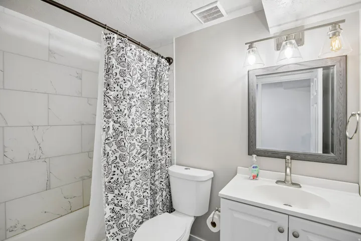 Bathroom featuring a white vanity with integrated sink, brushed nickel faucet, framed mirror, three-light vanity fixture, and tiled shower surround