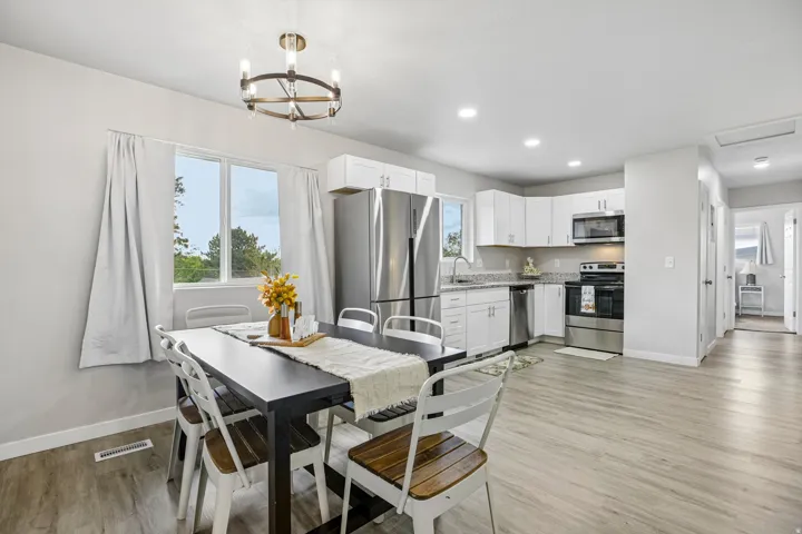 Open concept layout with wood-finish flooring, white cabinetry, stainless steel appliances, and recessed lighting