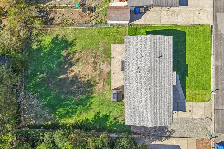 Gable roofline, expansive grass yard, concrete patio, concrete driveway, and mature landscaping
