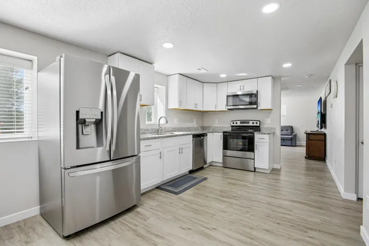 Kitchen featuring white cabinetry, light-toned countertops, stainless steel appliances, and wood-finish flooring