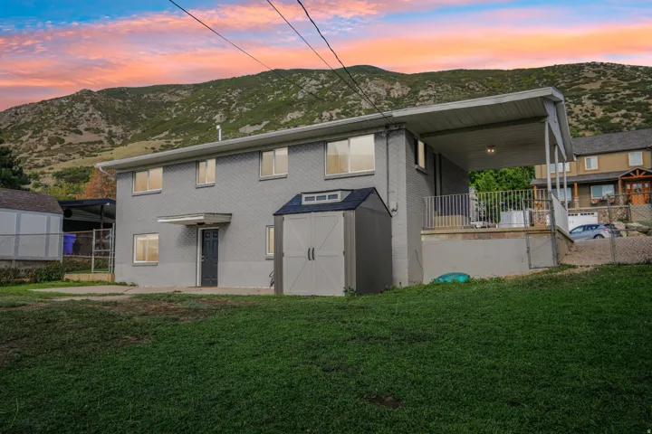 Two-story exterior with a covered carport, elevated patio with metal railings, and a storage shed