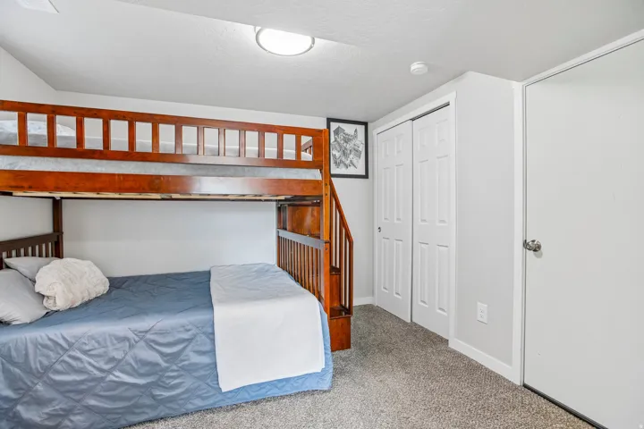 Carpeted room featuring a built-in wooden bunk bed structure with an integrated staircase, white bi-fold closet doors, a white solid door, and a flush-mount ceiling light fixture