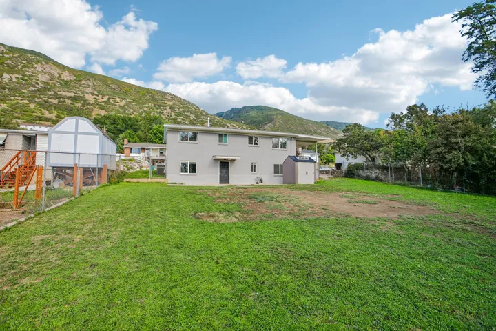 Expansive grass yard with a mountain backdrop, featuring a two-story residence, chain-link fencing, and an outdoor storage shed