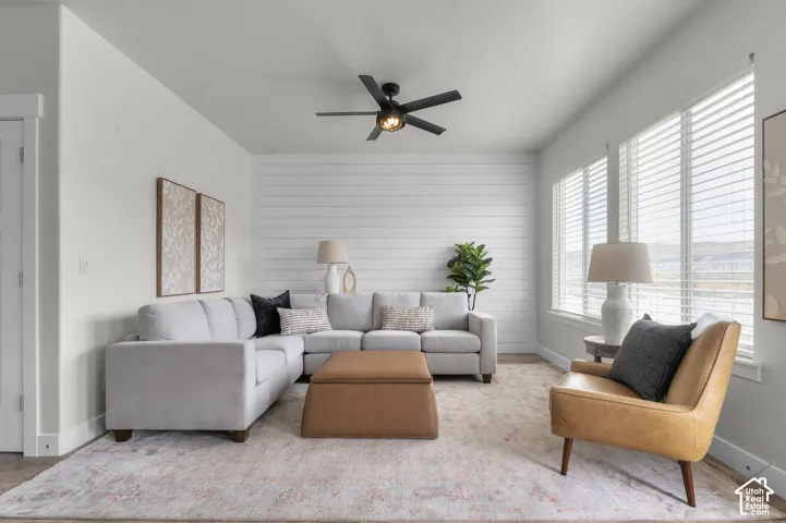 White wall finishes, wood-finish flooring, multiple large windows with blinds, shiplap accent wall, and a ceiling fan with integrated lighting