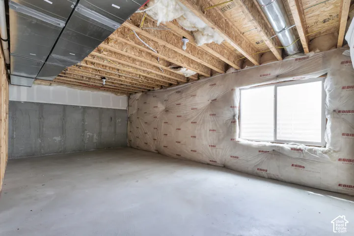 Unfinished space featuring an exposed wood joist ceiling, concrete walls, and a window for natural light