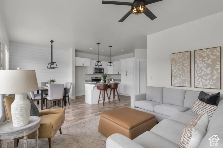 Open-concept living space featuring wood-finish flooring, a contemporary ceiling fan, recessed lighting, and a kitchen island with seating