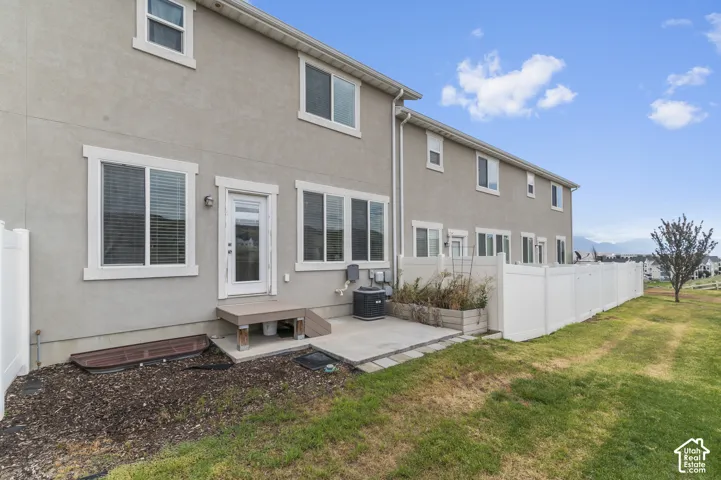 Exterior stucco finish, white frame windows, glass-paneled door, concrete patio, and a white privacy fence
