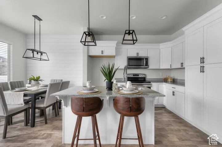 White shaker cabinetry with dark hardware, granite countertops, stainless steel appliances, and wood-finish flooring