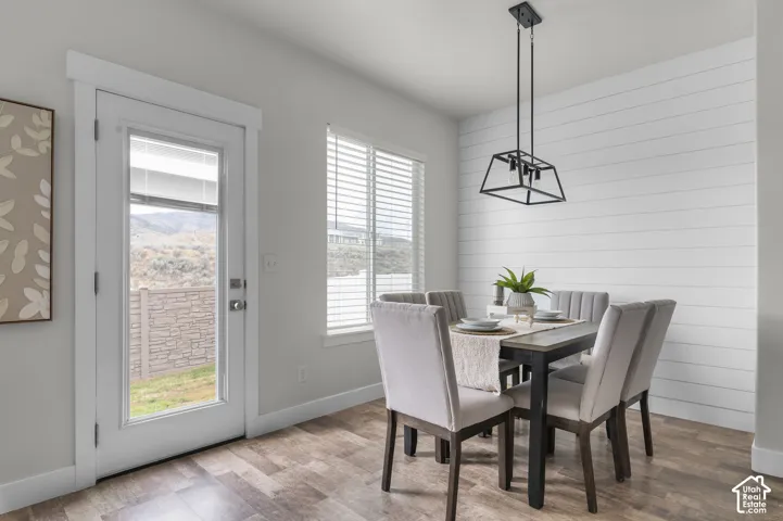 Wood-finish flooring, white shiplap accent wall, modern black geometric light fixture, white window blinds, and a full-light exterior door