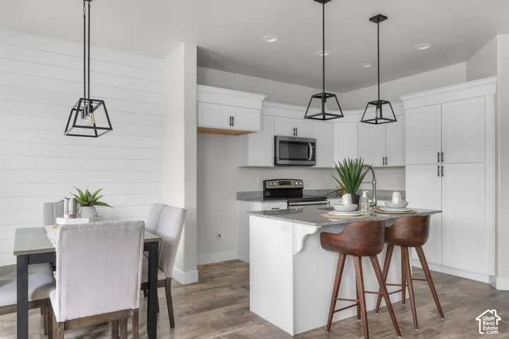 Spacious kitchen featuring white cabinetry, stainless steel appliances, a center island with counter seating, and wood-finish flooring