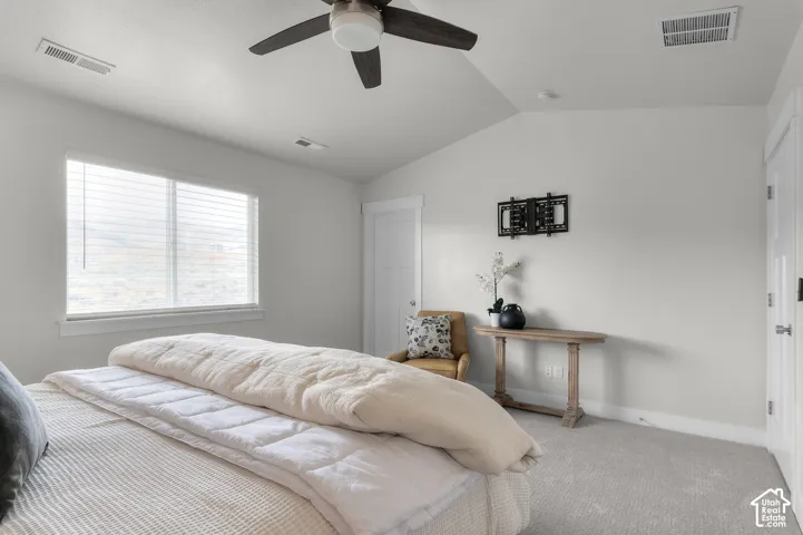 Vaulted ceiling with a ceiling fan, large window with blinds, light-colored carpeting, and a wall-mounted television bracket