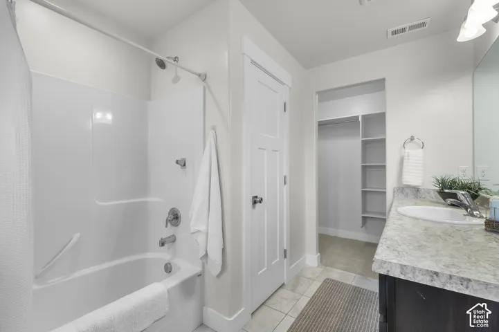 Tub and shower combination with chrome fixtures, vanity with integrated sink, patterned countertop, and built-in closet shelving