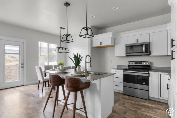 Kitchen featuring white cabinetry, stainless steel appliances, granite countertops, a center island with a sink, and wood-finish flooring