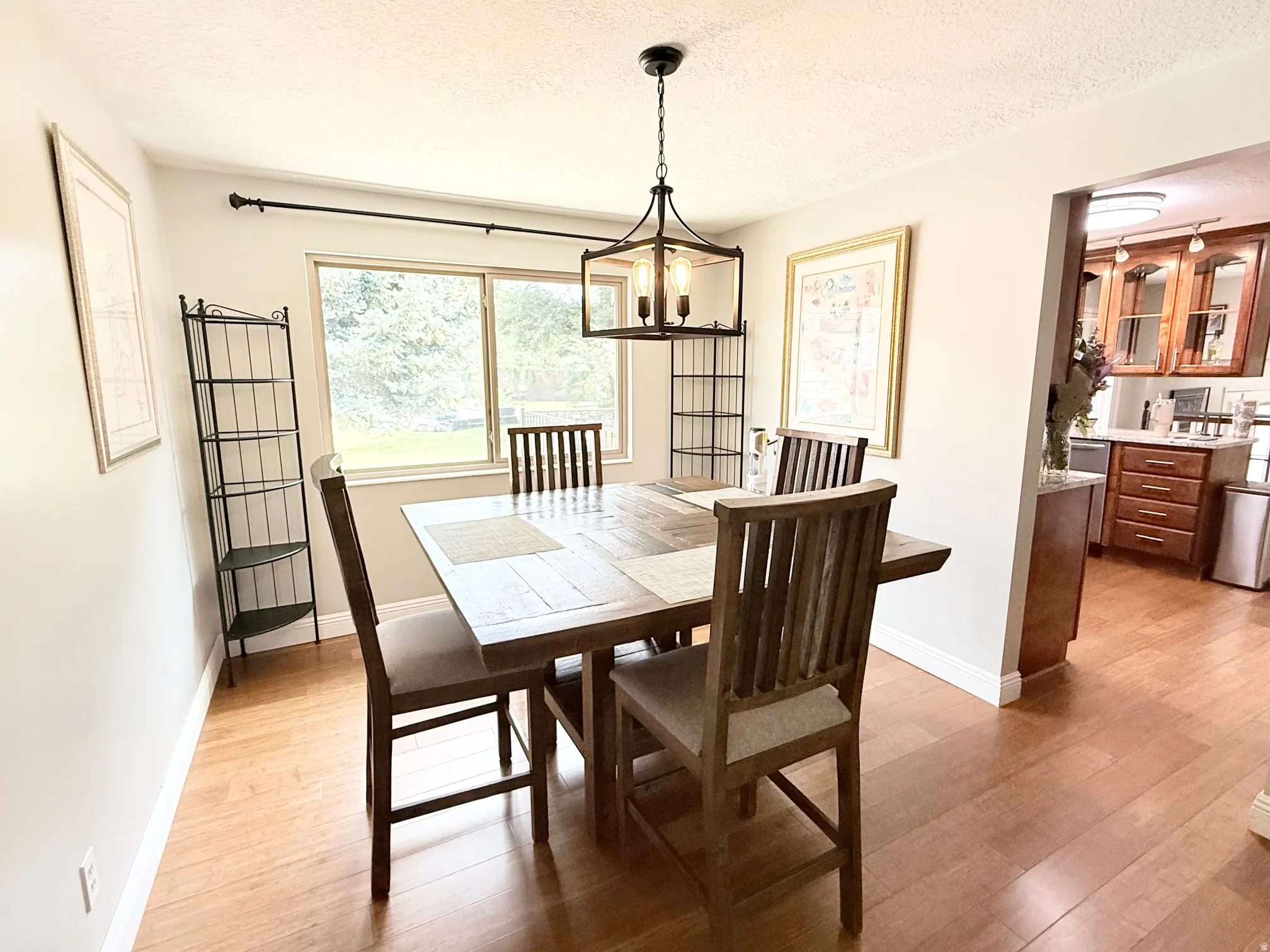 Hardwood-style flooring throughout, featuring a dining area with a contemporary chandelier, large picture window, and a pass-through opening to the kitchen