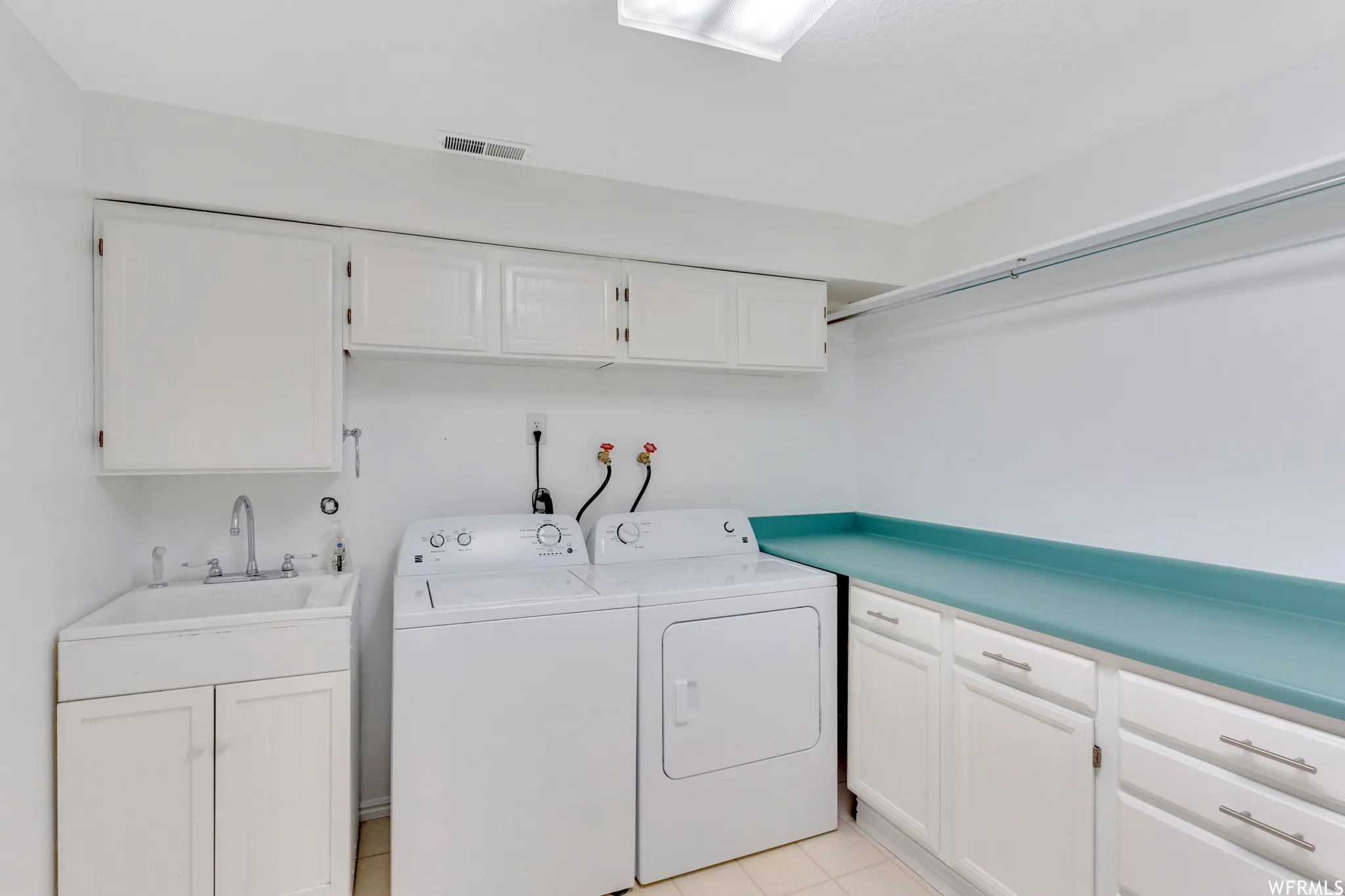 Built-in utility sink with white cabinetry, upper white storage cabinets, and a light blue countertop with additional lower cabinetry