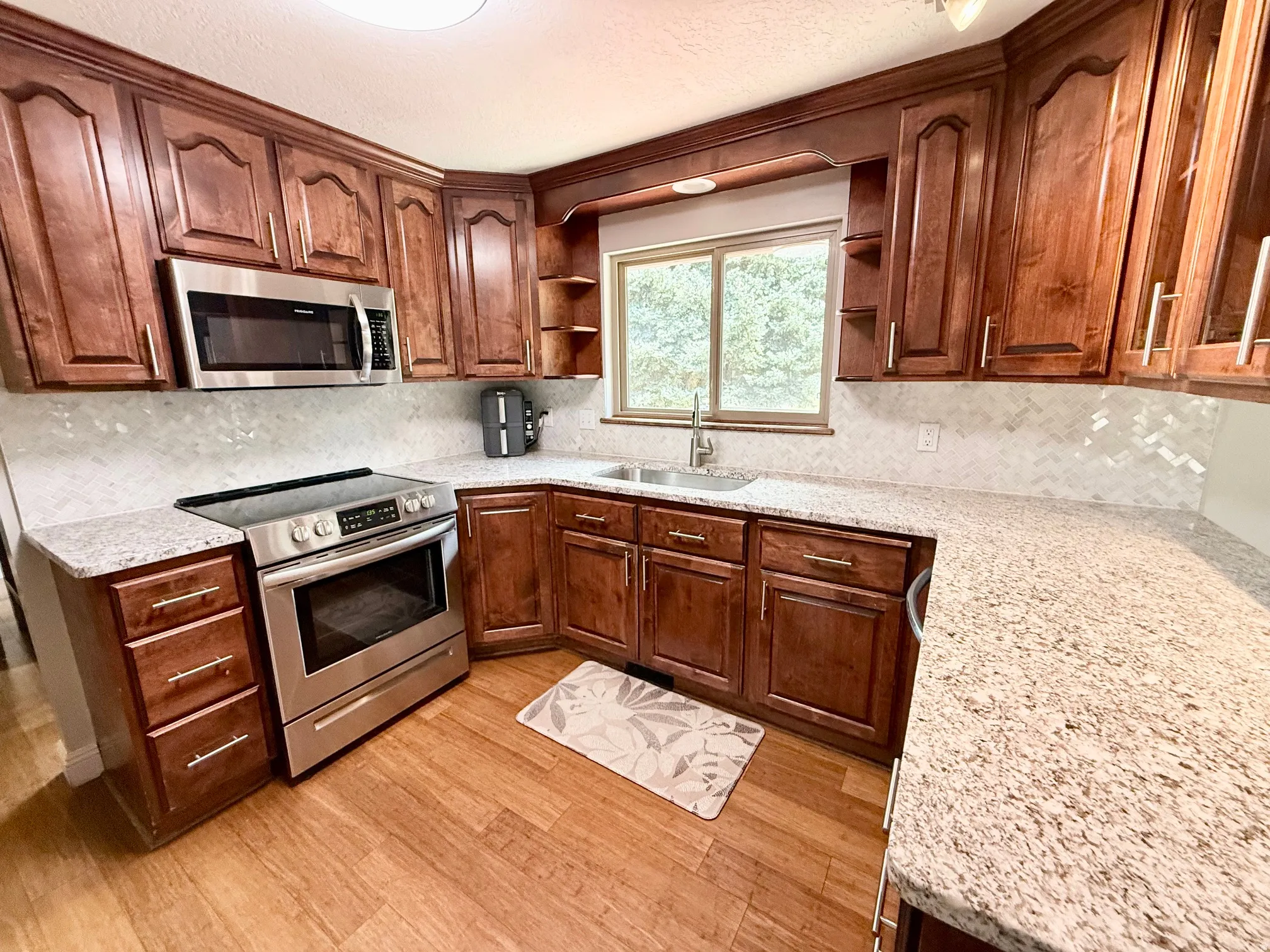 Warm wood cabinetry with brushed nickel hardware, stainless steel appliances, granite countertops, and a full-height tile backsplash