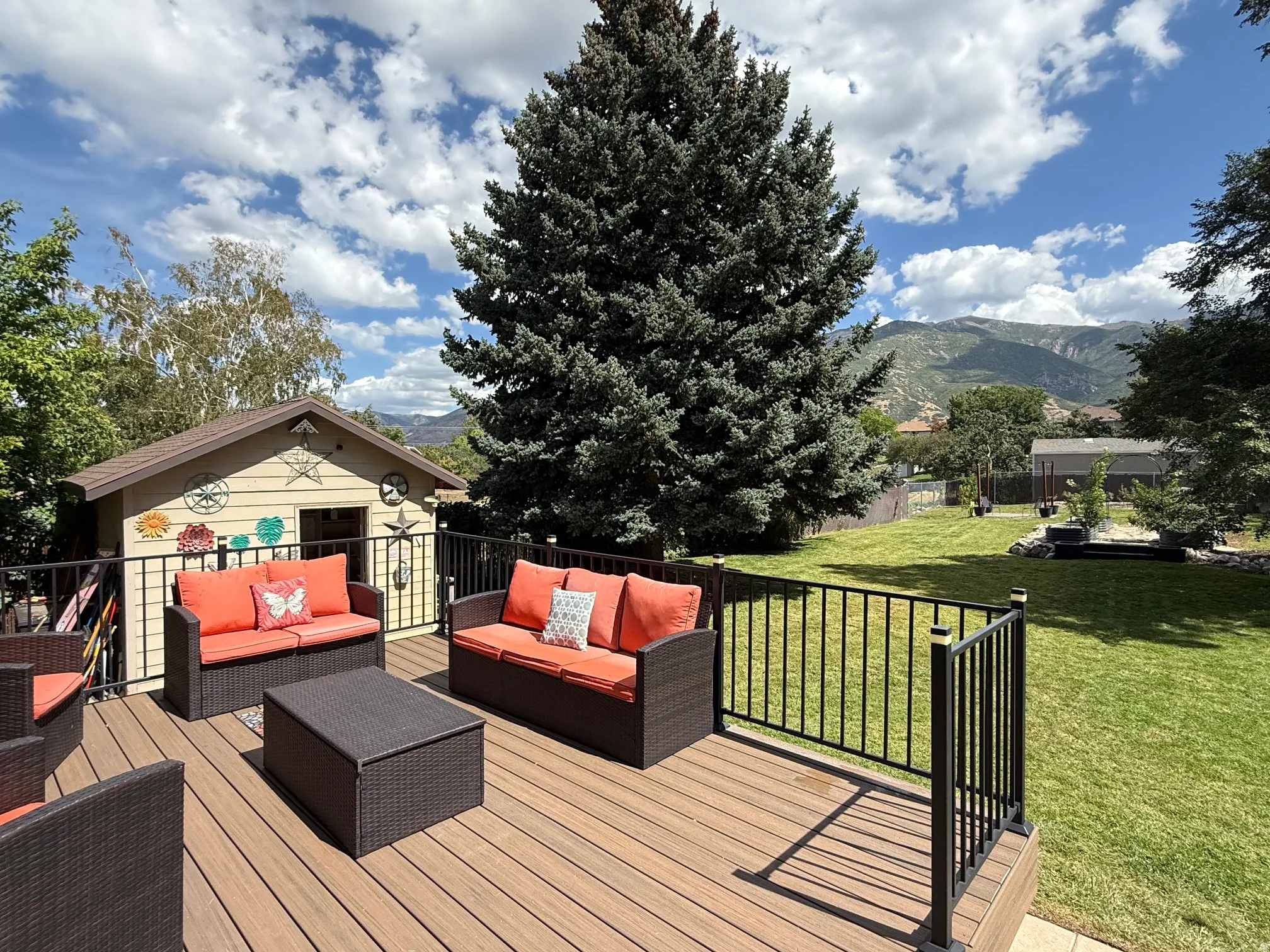 Expansive wood-finish deck with black metal railings, overlooking a large grassy yard with mature trees