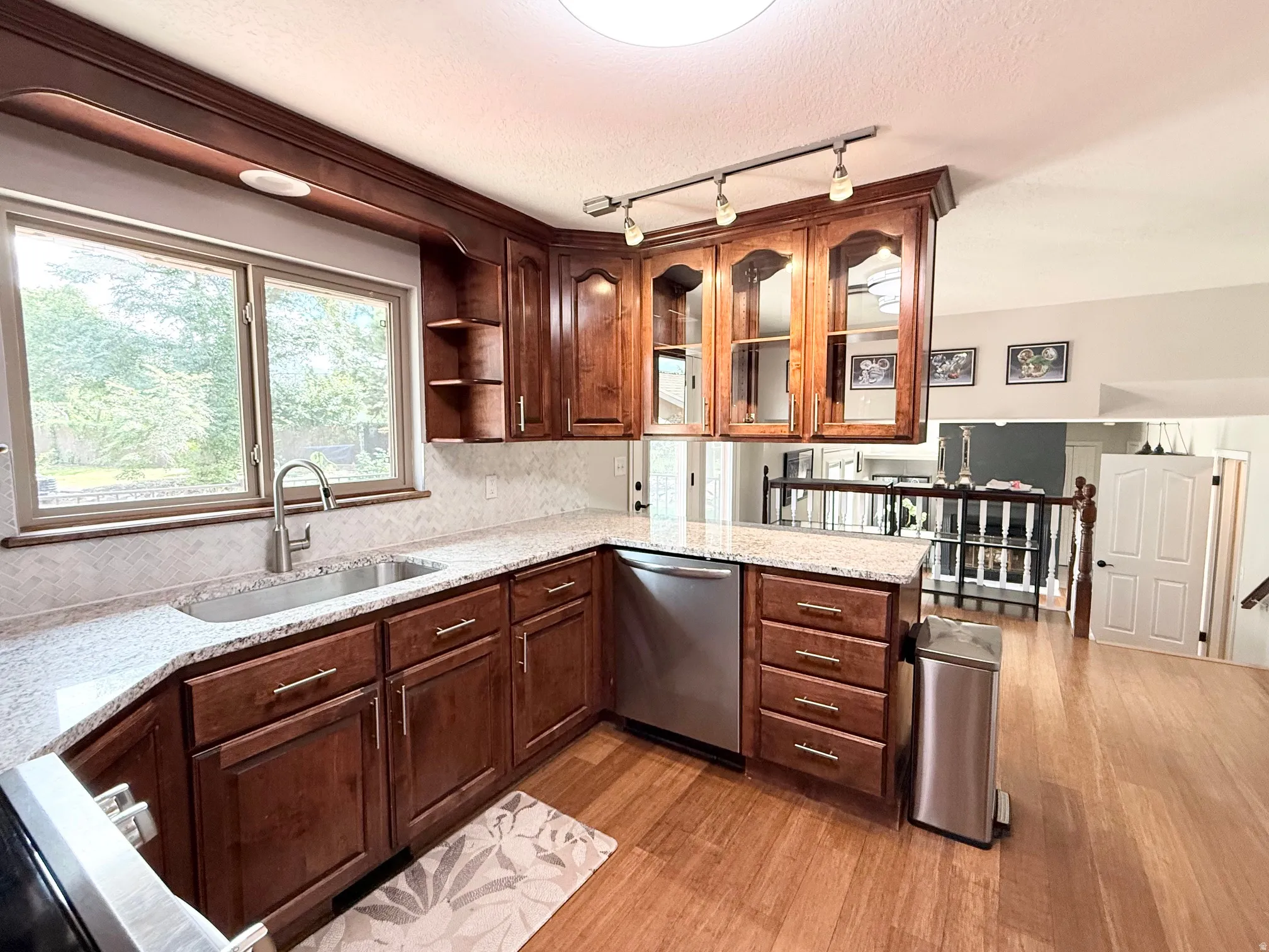 Kitchen featuring wood-finish flooring, a stainless steel sink, wood cabinetry, stone countertops, and a tile backsplash
