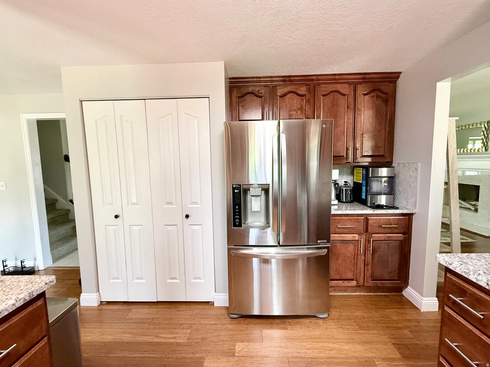 Wood-finish flooring, cherry-toned cabinetry, stainless steel refrigerator, granite-look countertops, and white bifold doors