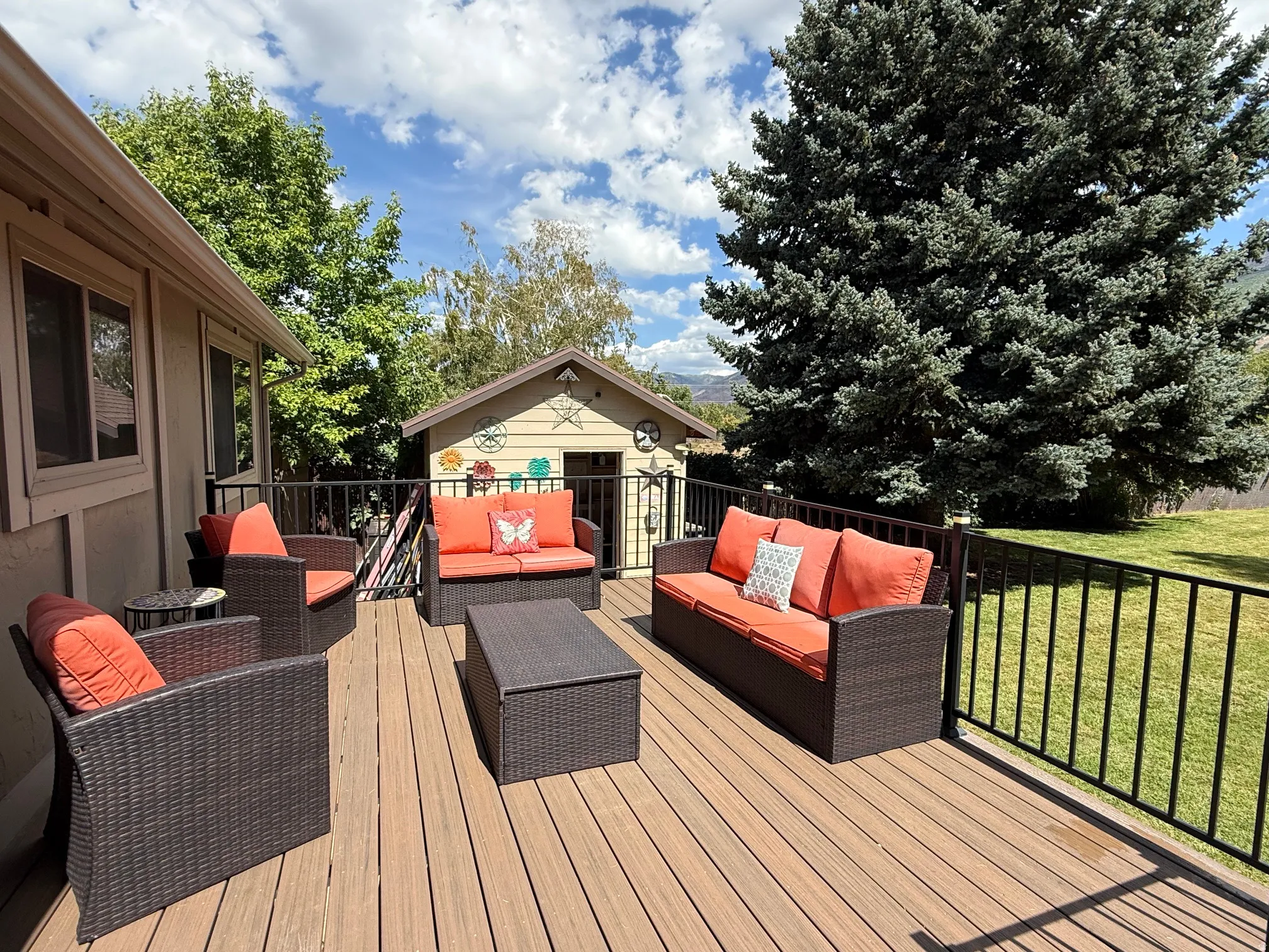 Spacious outdoor deck with composite decking and black metal railings, featuring a detached shed and expansive green lawn