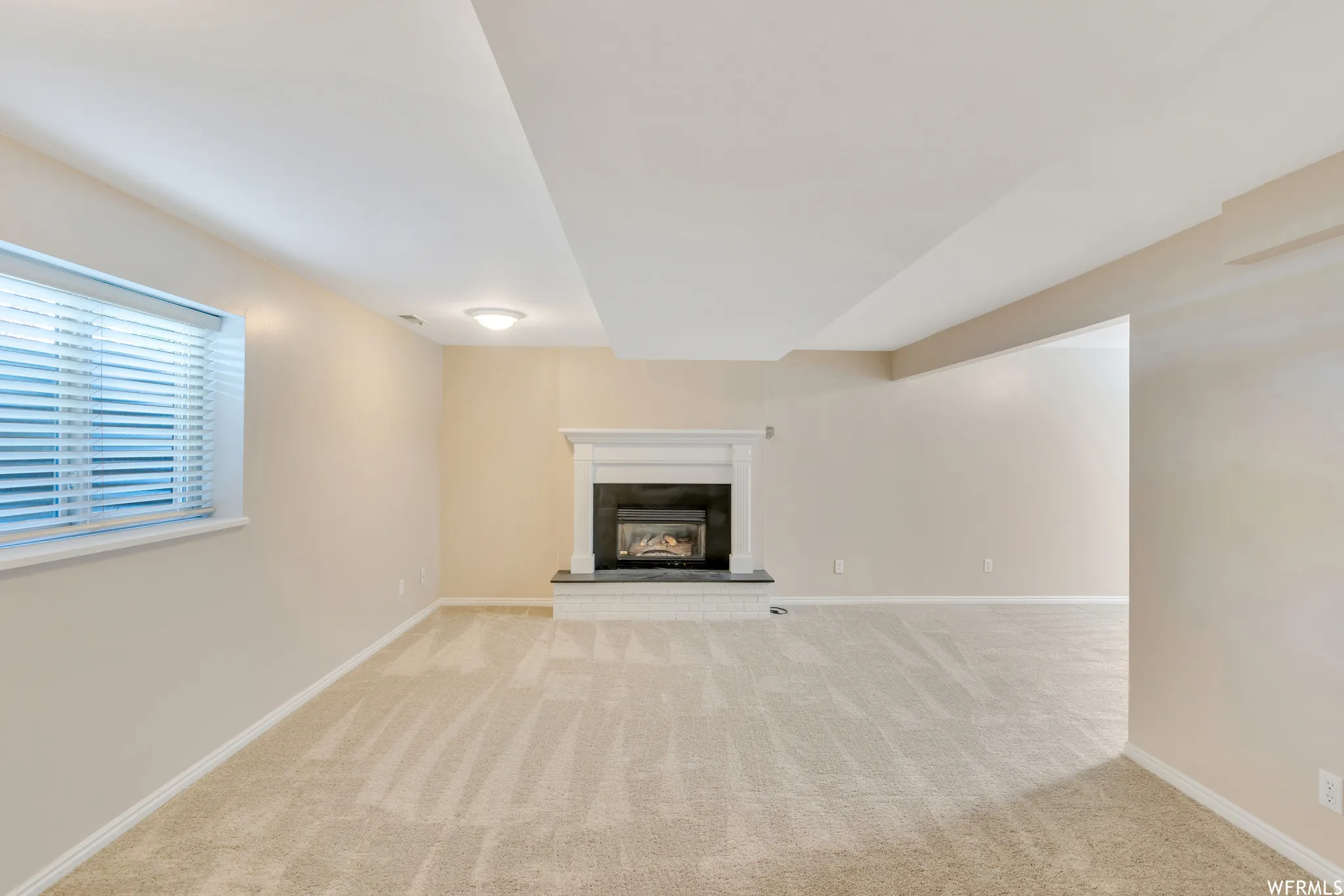 Integrated fireplace with white mantel and dark surround, plush carpet flooring, recessed lighting, and a window with blinds